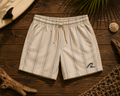 Coastal Stripe Shorts flat lay on timber showing cream linen pinstripe and embroidered wave logo