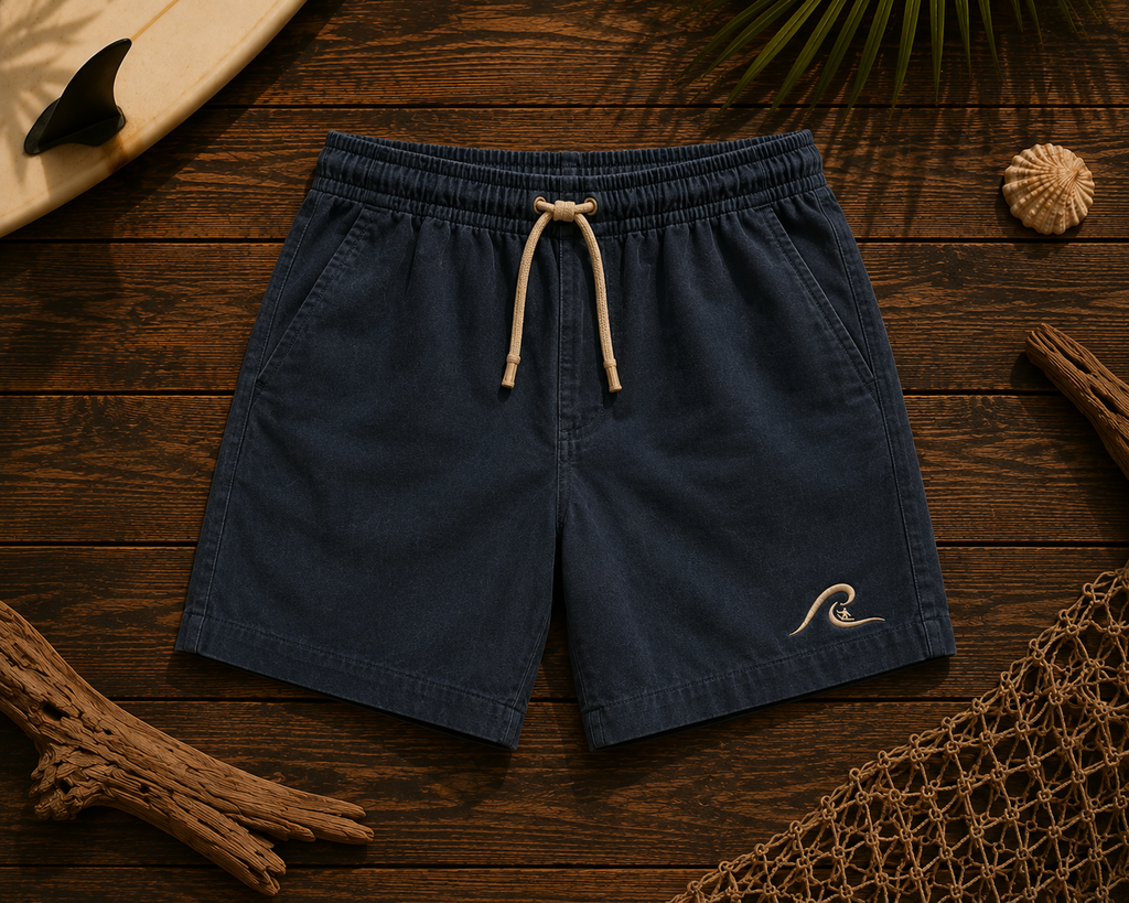 Ocean Fade Shorts flat lay on timber showing washed navy fabric and embroidered wave logo