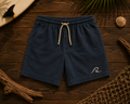 Ocean Fade Shorts flat lay on timber showing washed navy fabric and embroidered wave logo